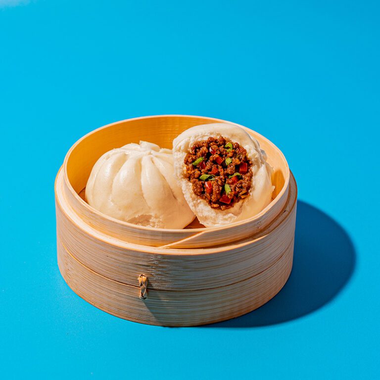 Bao in a wood bao steamer container on a vibrant blue backdrop